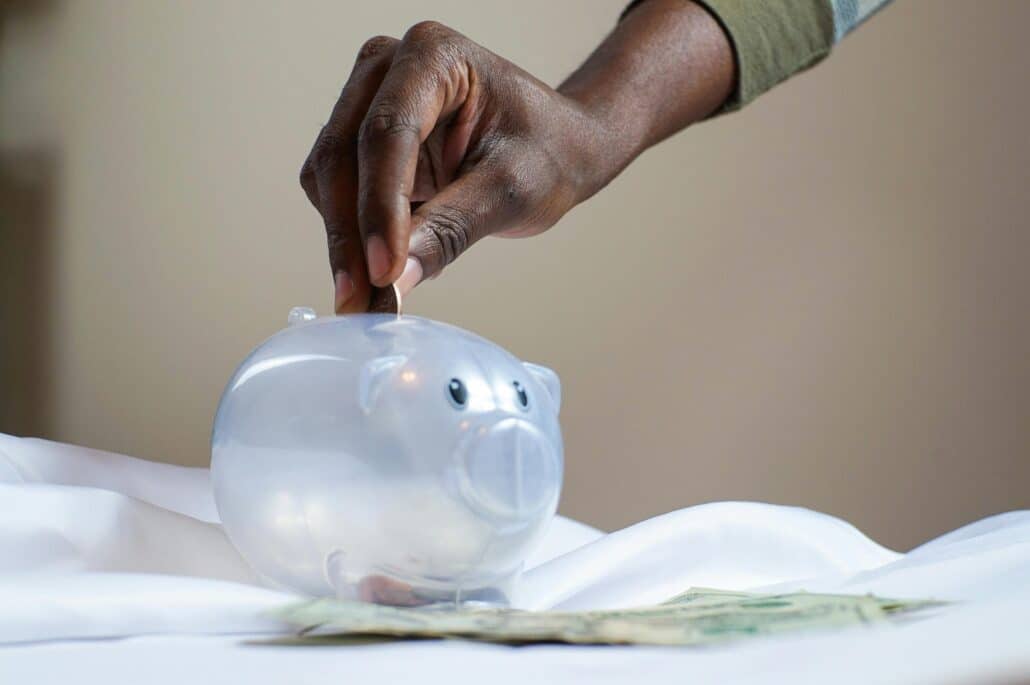 person putting coins into a clear piggy bank