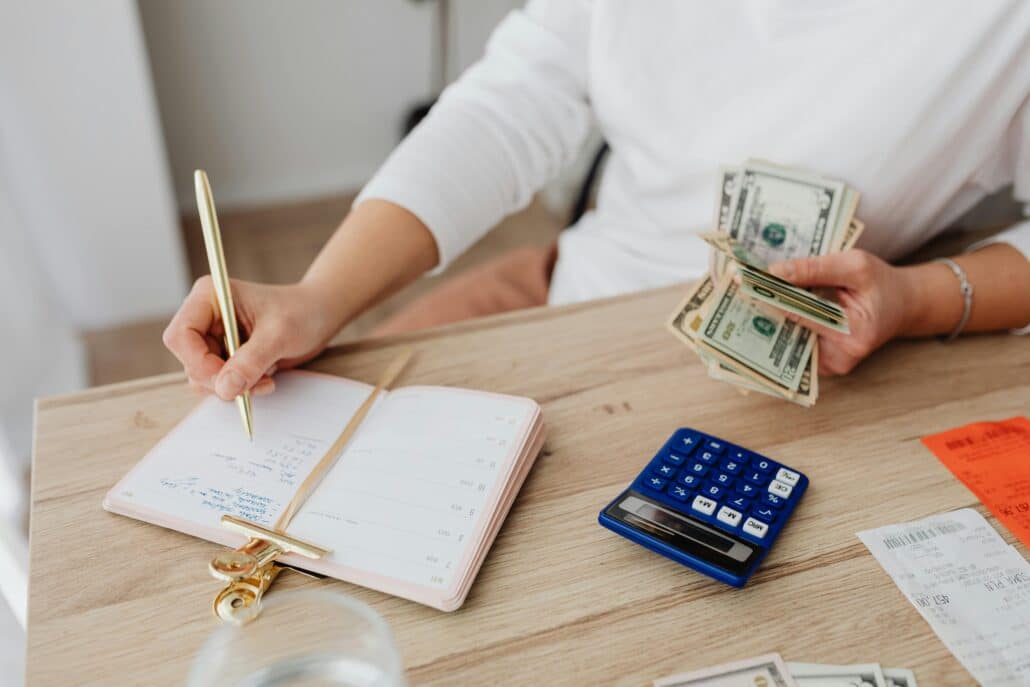 someone taking notes while holding a wad of cash and using a calculator