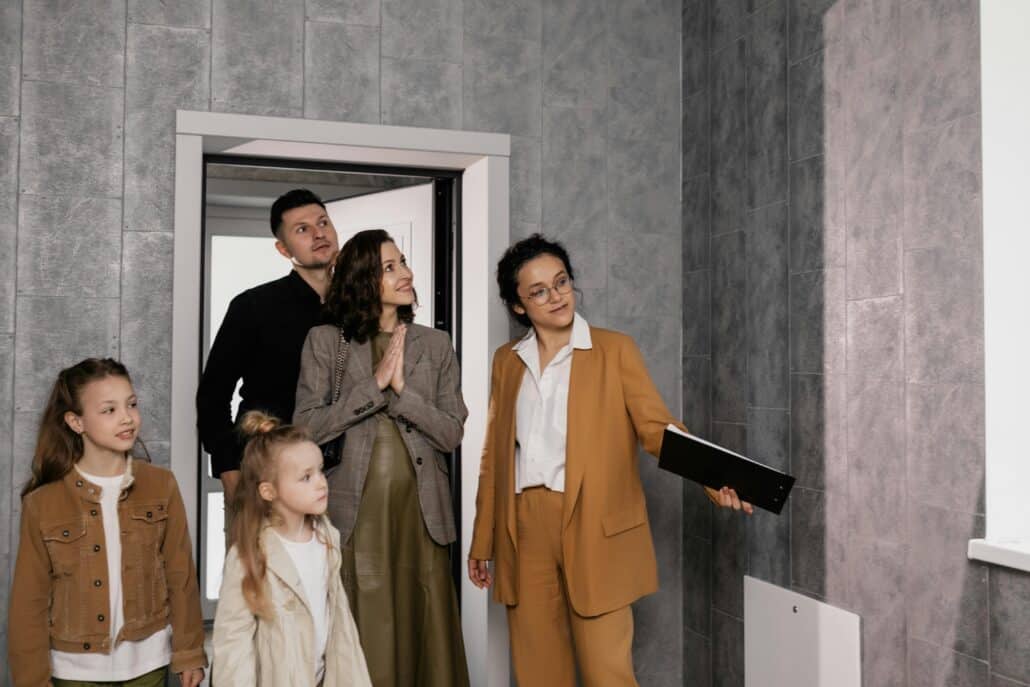 woman in glasses and tan suit showing a family of four through a house