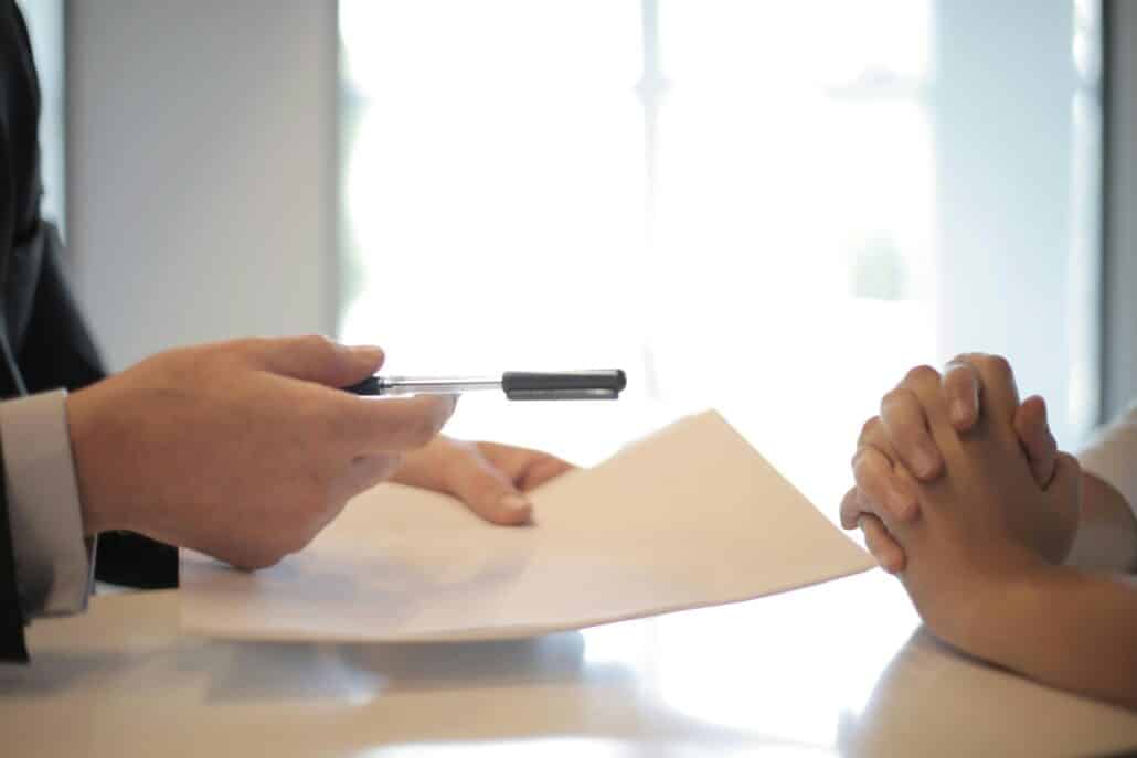 someone handing over paper and a pen across a table