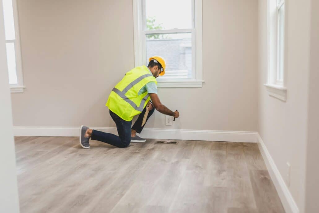 a man in a hard hat and neon vest shining a flashlight into a floor drain