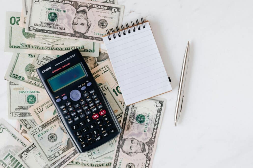 cash spread out on a table with a calculator, notepad, and pen on top