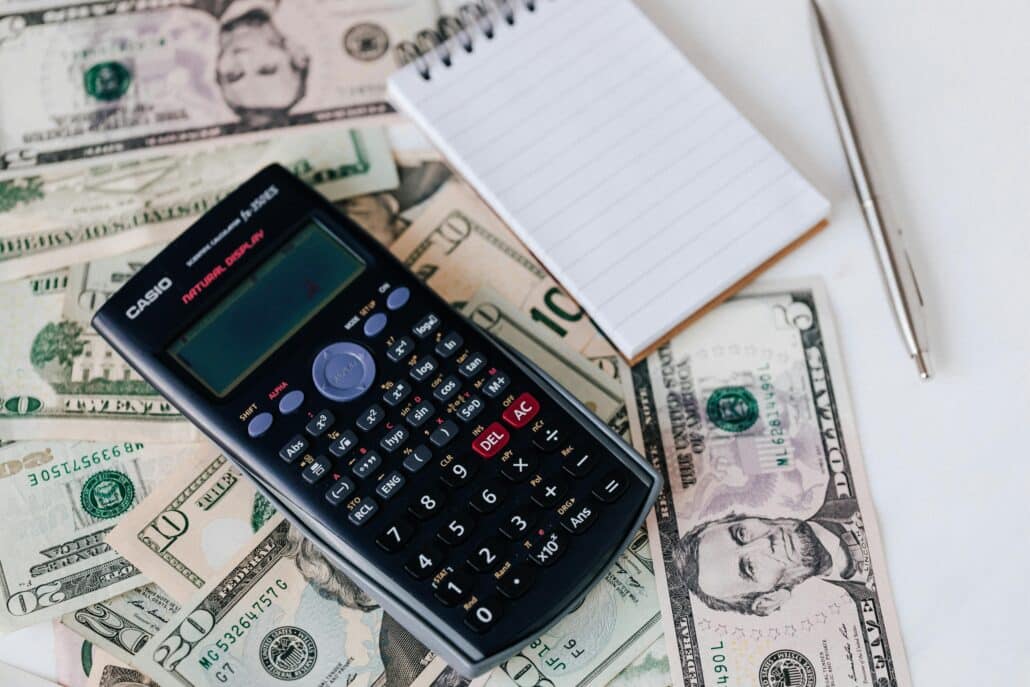 a calculator, notepad, and pen over a pile of cash