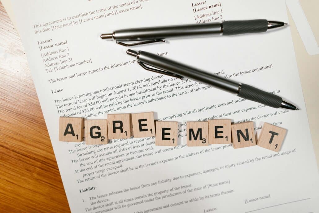 Scrabble tiles spelling out the word "agreement" on top of a lease agreement and two black pens