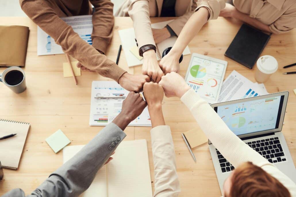 people putting hands together in the center of a table covered in papers with graphs and the like